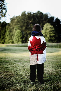 depth of field photography of boy wearing red maple leaf-printed top facing tall green leafed trees thumbnail
