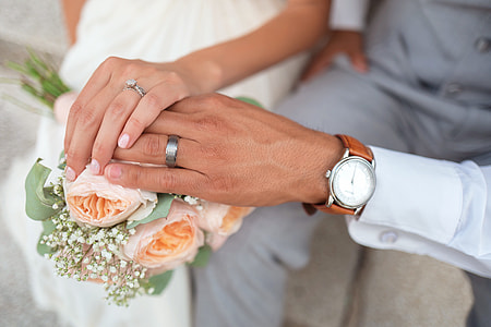 female and male holding each others hand showing their wedding rings while touching flowers thumbnail