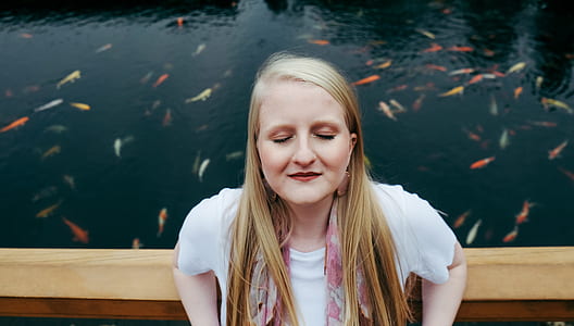 closed eyes woman leaning on wall near body of water thumbnail