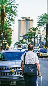 man wearing white polo shirt holding trolley bag near silver Chevrolet truck staring at distance over beige building thumbnail
