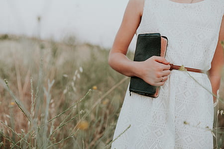 woman holding black book walking on tall grasses thumbnail