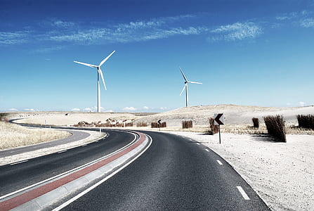 two white windmills near gray concrete road under blue sky thumbnail