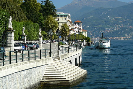 yacht on body of water near concrete road and mountain range thumbnail