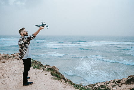 person holding drone standing on rock near ocean thumbnail
