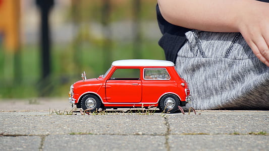 red and white 3-door hatchback scale model toy beside sitting person during daytime thumbnail