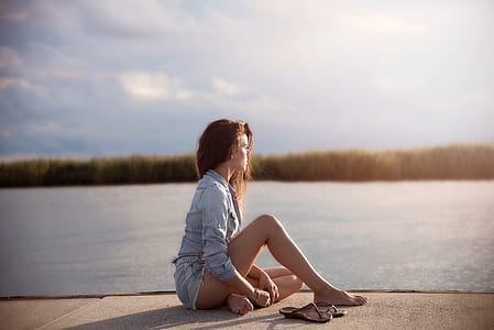 Woman In Blue Denim Jacket Sitting Near Body Of Water thumbnail