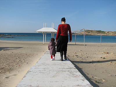adult holding toddler's hand while walking on gray pathway thumbnail