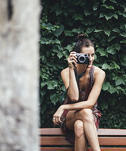 woman holding camera while sitting on brown wooden bench outdoor thumbnail
