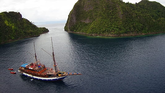 Brown Ship Near Mountain Covered With Green Trees thumbnail