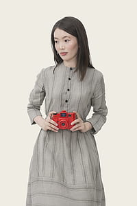 woman wearing long-sleeved dress holding red camera while standing thumbnail