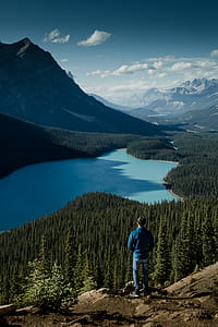 man standing on hill in front of lake across mountain during daytime thumbnail