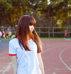 woman in white and red crew-neck t-shirt standing on track field during daytime thumbnail