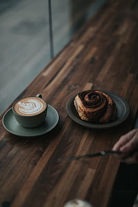 rolled bread on round black plate beside teacup filled with coffee on round gray ceramic saucer thumbnail