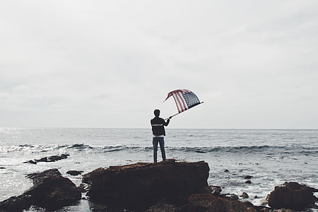 person holding American flag near on the body of water thumbnail