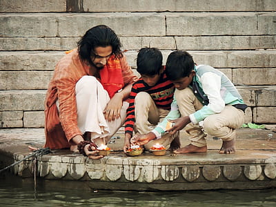 man and two boys sitting holding candles beside body of water thumbnail