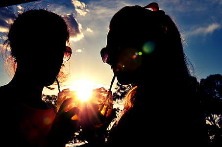silhouette of two women zipping drinks during golden hours thumbnail