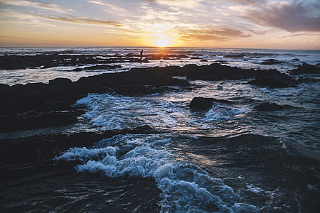 person standing on rock seashore during golden hour thumbnail
