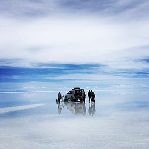 gray SUV on body of water with group of people under cloudy sky thumbnail