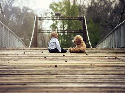 boy sitting beside brown bear plush toy thumbnail
