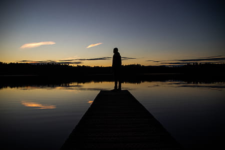 Silhouette of Person Standing on Body of Water Dock during Sunrise thumbnail