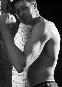 grayscale photo of standing man leaning beside on wall thumbnail