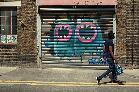 Street photo of a London man with a shopping bag. East London street art can be seen in the background thumbnail