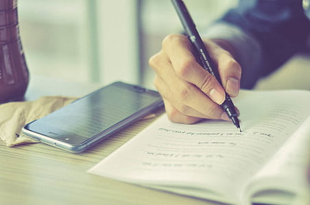 person holding black ballpoint pen beside black smartphone on table thumbnail