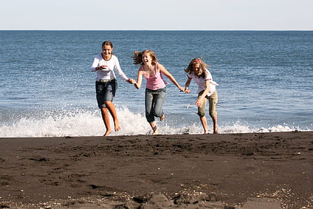 three girls running away from ocean wave on the beach thumbnail