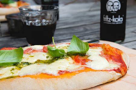 Pizza Top With Green Leafy Vegetable Near Glass of Black Liquid thumbnail