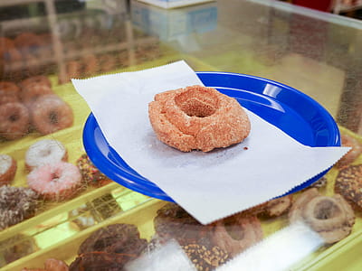 A cinnamon cake donut sitting on a blue plate inside of a donut shop. thumbnail