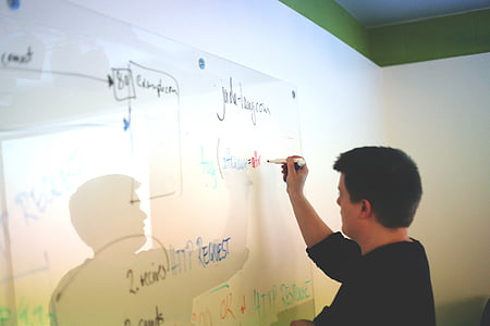 man in black shirt writing on whiteboard inside room thumbnail
