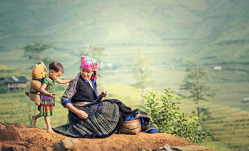 selective focus photography of girl carrying bear plush toy near woman sitting on hill thumbnail