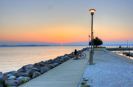 person sitting on bench facing body of water thumbnail
