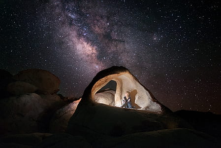person sitting on rock formation under starry sky thumbnail