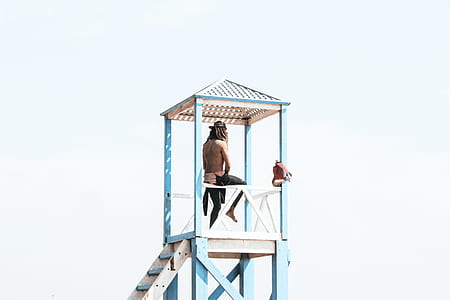 person sitting on blue watch tower during daytime thumbnail