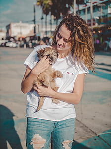 woman in white shirt and distressed blue denim bottoms holding long-coated tan puppy during daytime thumbnail