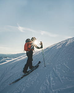 man wearing skis walking up snow covered hill during day thumbnail