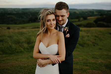 photo of woman in sweetheart neckline dress with man in black suit jacket, black necktie, and white dress shirt with green grass in the background thumbnail