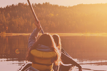 two women riding boat while holding oar on body of water thumbnail