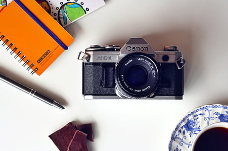 black and gray Canon camera near orange notebook and black click pen thumbnail