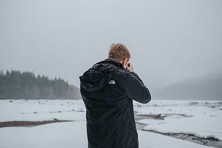 man wearing black jacket while taking photos on icy field thumbnail