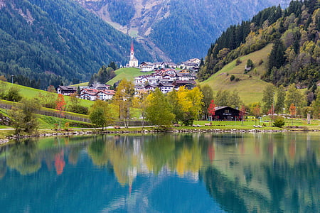 photo of calm body of water near village and mountains at daytime thumbnail
