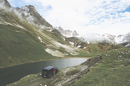 black Jeep Wrangler parked near river and ice capped mountains during cloudy day thumbnail