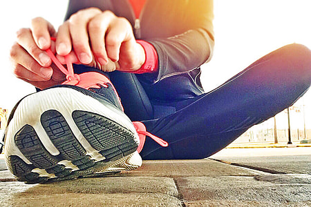 woman tying her shoe lace sitting on the gray concrete pavement thumbnail