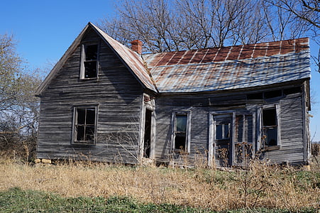 abandoned gray wooden house surrounded by withered trees and grass during daytime thumbnail