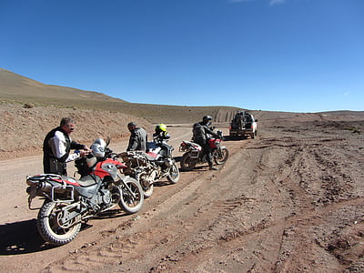 three man beside dual sports motorcycle on dirt road during daytime thumbnail