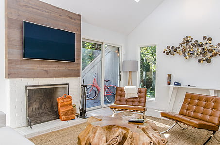interior photography of living room with two tufted brown leather Barcelona chairs beside brown slab coffee table near fireplace under flat screen TV thumbnail