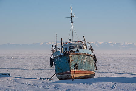 grey and brown fishing boat on snow under blue sky thumbnail