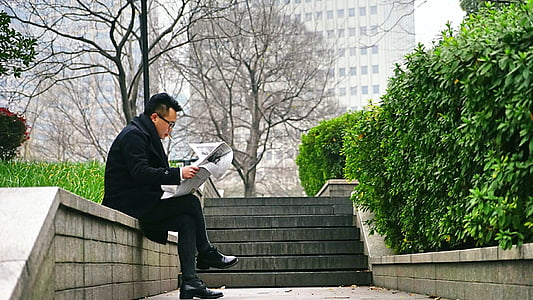man wearing black coat while reading newspaper thumbnail