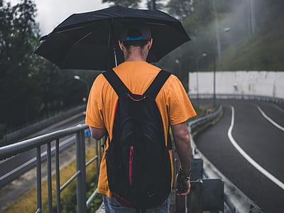 Man Wearing Orange Shirt Holding Black Umbrella thumbnail